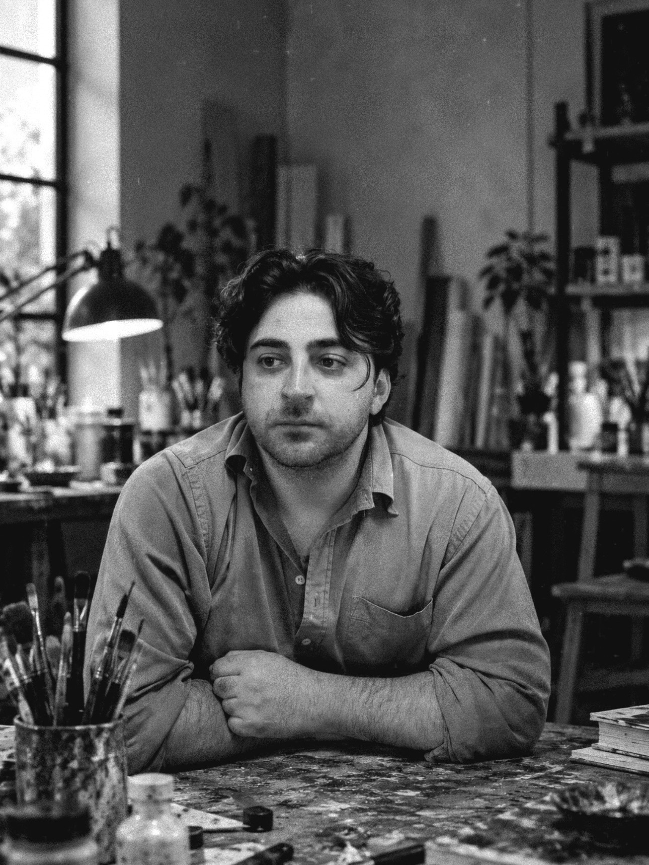 Black-and-white portrait of the artist in the studio, among brushes and paint-stained tables
